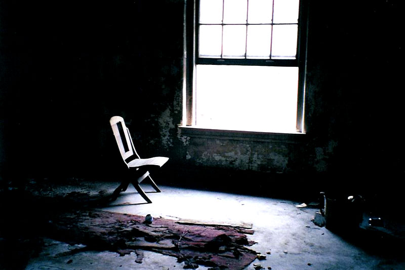 A chair in an abandoned building, next to an open window with bright light streaming through. Escape(Window), photo by lj beautiful_umbra
